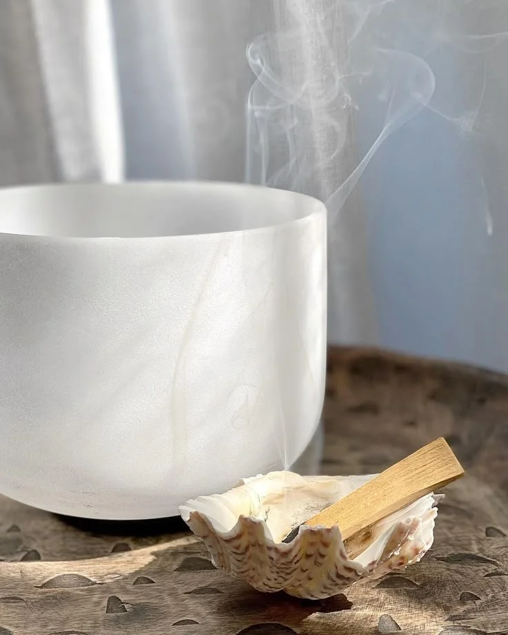 A white ceramic bowl and conch shell on a wooden altar surface.