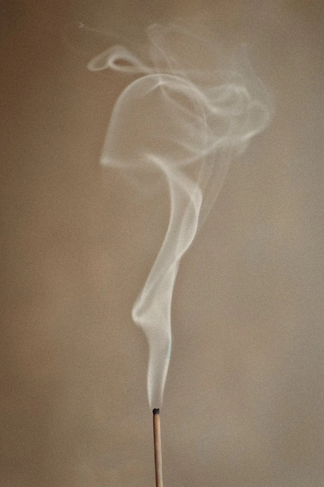 Incense smoke rising in soft swirls against a warm background.